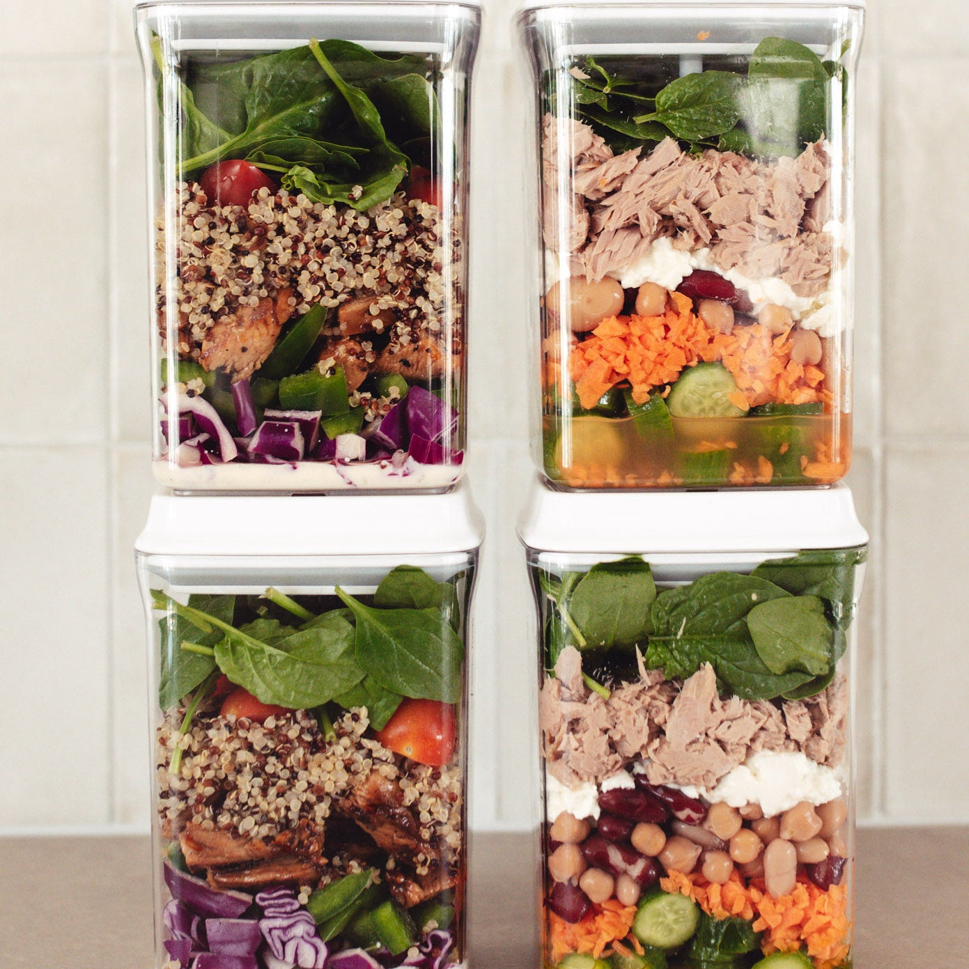 Four stacked containers with pre-made salads on a neutral background