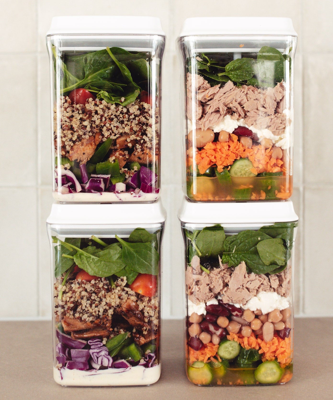 Four stacked containers with pre-made salads on a neutral background
