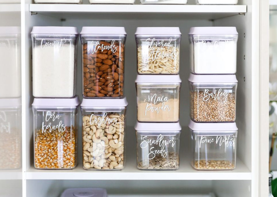 Set of labeled storage containers with various seeds and grains on a shelf.
