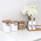 white laundry countertop with laundry jars labelled "washing powder" "Napisan" and "pegs" with two pump bottles in a bamboo container labelled "hand cream" and "hand soap"