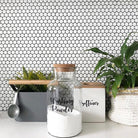 Custom vinyl laundry labels on glass jars with washing powder and softener, set against a white tiled background with green plants.